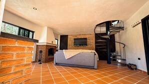 Amplia sala de estar con chimenea, un sofá gris, un televisor montado en una pared de ladrillo y una escalera de caracol.