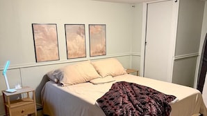 A bedroom with a bed, a bedside table with a lamp, a rug, and three framed pictures on the wall. - Serene 2-bedroom apartment in Astoria perfect for your getaway (Astoria)