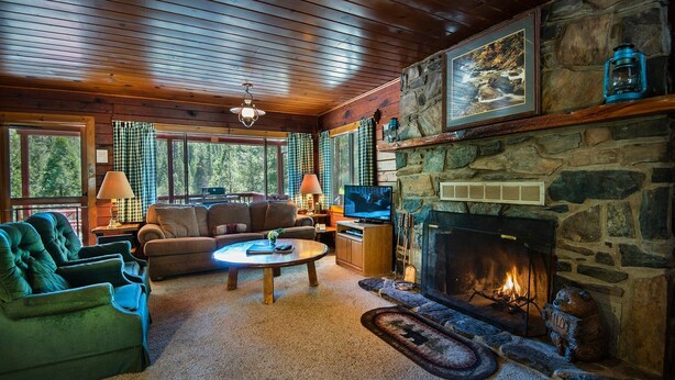 Un intérieur de chalet chaleureux avec une cheminée en pierre, un téléviseur et un coin salon confortable.