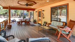 Une terrasse en bois, meublée pour l’extérieur, dotée d’un ventilateur de plafond et offrant une vue sur la forêt environnante.