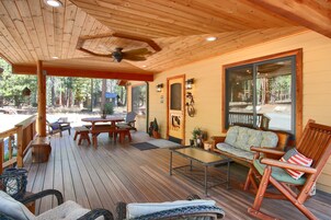 Um deck de madeira com móveis de exterior, um ventilador de teto e vista para a floresta ao redor.