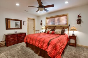 Quarto com cama, cômoda, mesa de cabeceira, ventilador de teto e janela com persianas.