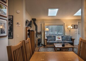 Een gezellige woonkamer met een open haard, een bank, een eettafel en een dakraam.