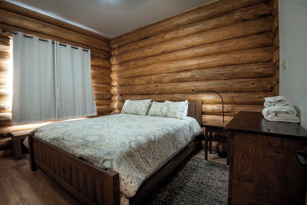 Camera da letto in una baita di legno con un letto, una scrivania e una sedia.