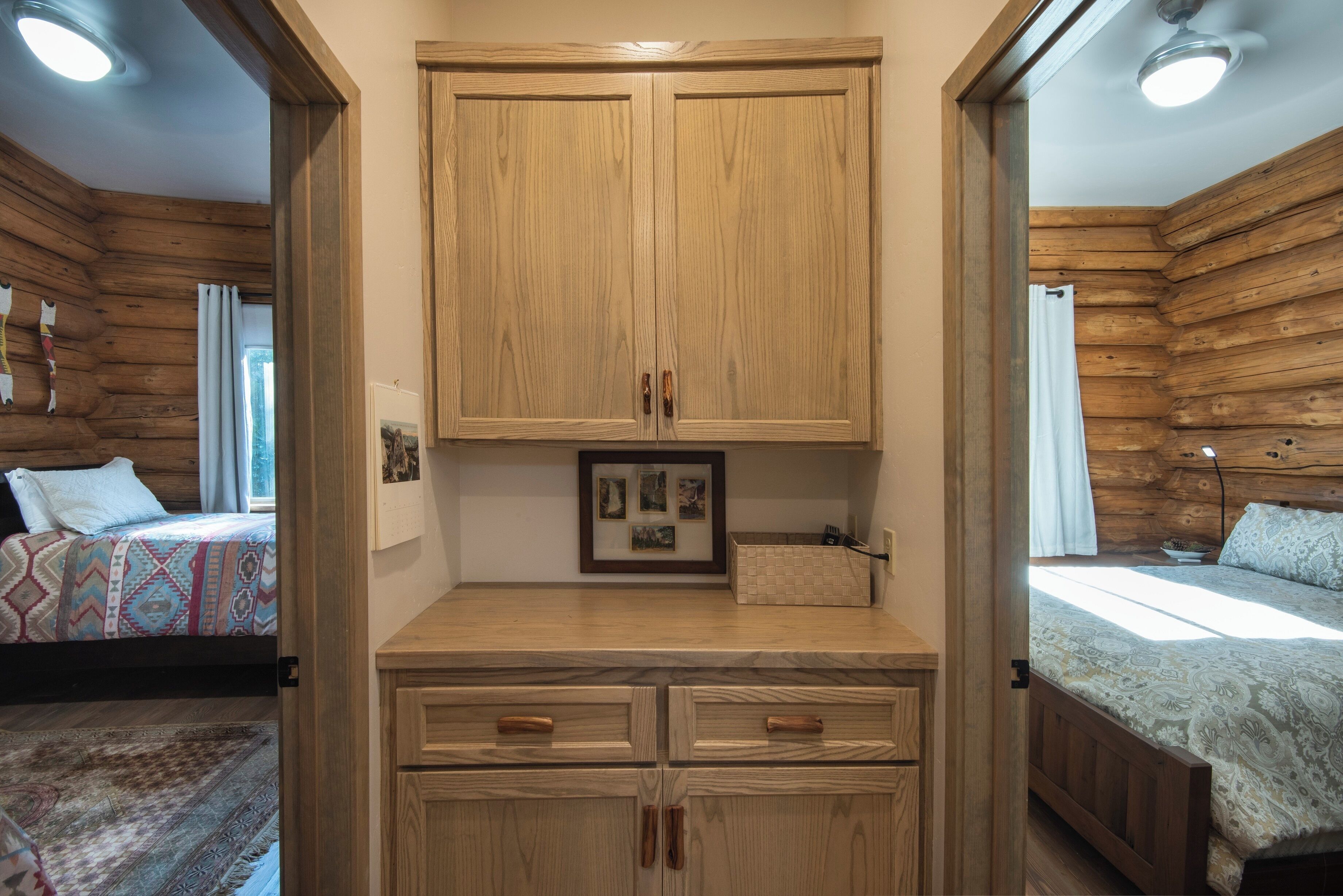 A wooden cabin interior with a central cabinet, two beds, and a small table with a picture frame.