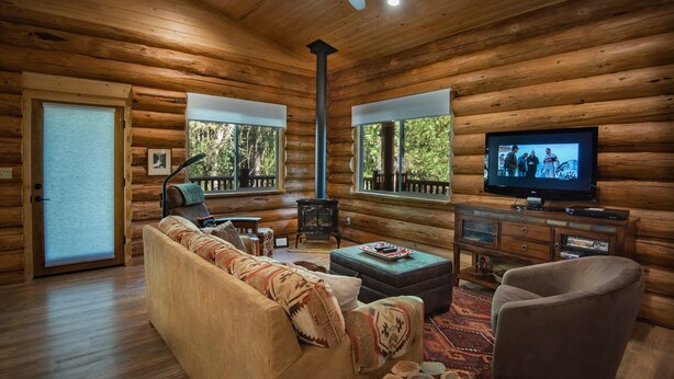 A log cabin interior with a sofa, ottoman, television, and a fireplace. - The Mini Cabin (Yosemite National Park)