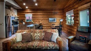 A log cabin interior with a sofa, dining table, chairs, and a kitchen area. - The Mini Cabin (Yosemite National Park)
