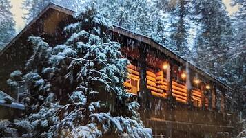 A log cabin with a snow-covered exterior and a warm interior light.