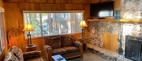 A cozy living room with wooden walls, a stone fireplace, a television, and two lamps.