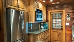 A kitchen with wooden cabinets, stainless steel appliances, granite countertops, and a wooden door with a window. - Sugar Pine Suite (Yosemite National Park)