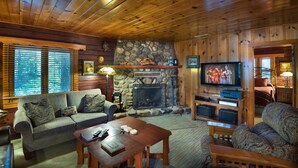 A cozy cabin interior with a stone fireplace, wooden walls, a television, and a sofa. - Sugar Pine Suite (Yosemite National Park)