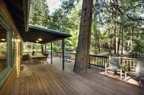 Een houten terras met buitenmeubilair, een pergola en uitzicht op een bebost gebied.