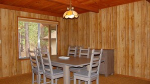 A dining area with a wooden table and chairs, a chandelier, and a view through a window. - Mountain Retreat (Yosemite National Park)