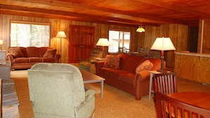 A cozy living room with wooden walls and ceiling, furnished with a sofa, chairs, and a coffee table. There are two lamps on side tables and a window providing natural light. - Mountain Retreat (Yosemite National Park)