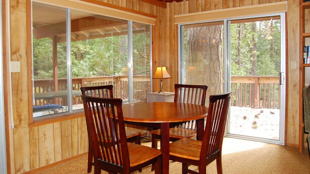 A wooden-paneled room with a round table and four chairs, large windows, and a sliding glass door leading to an outdoor deck. - Mountain Retreat (Yosemite National Park)