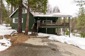 A green cabin with a covered porch, a staircase leading to a deck, and a snow-covered ground. - Grant's Camp (Yosemite National Park)