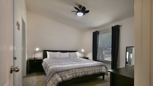 Ein Schlafzimmer mit einem Bett, zwei Nachttischlampen, einem Deckenventilator, einem Fenster mit Vorhängen und einer Kommode.