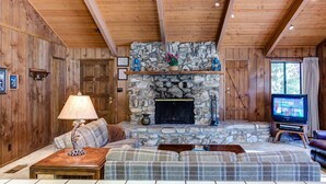 A cozy living room with a stone fireplace, wooden walls, a sofa, a coffee table, and a television. - Coyle's Cabin (Yosemite National Park)
