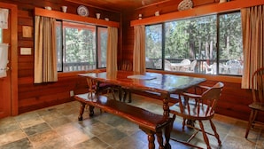 Interior de uma cabana de madeira com uma grande mesa de jantar, bancos e um ventilador de teto.