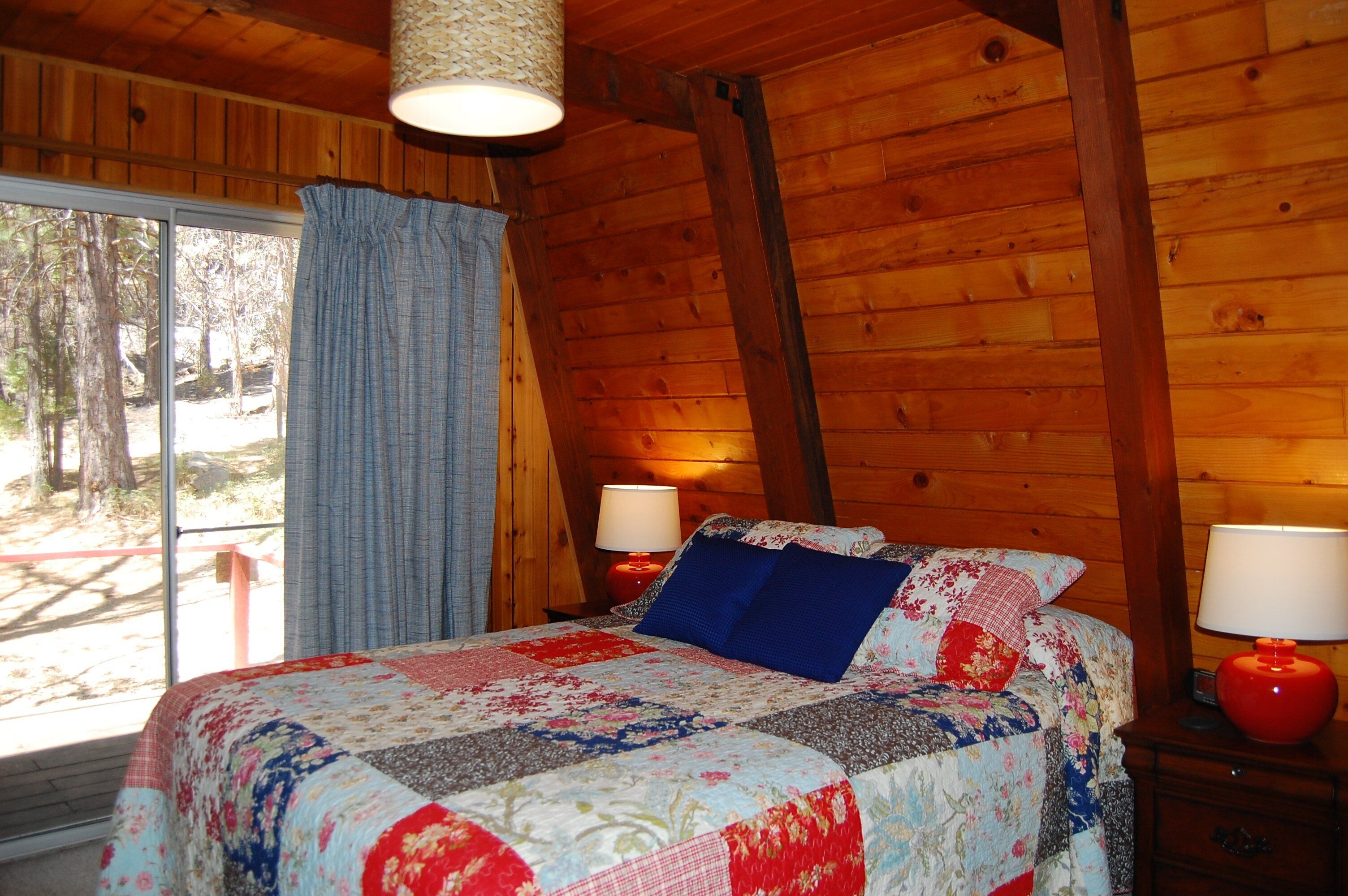 A wooden cabin bedroom with a large bed, two bedside lamps, and a window with curtains.