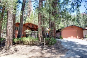 A cabin with a garage, surrounded by tall trees and a dirt driveway. - Mountain Memory (Yosemite National Park)