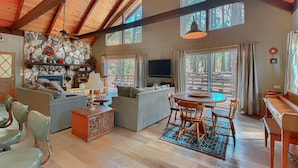 A spacious living area with a high ceiling, a fireplace, a television, and a dining table with chairs. - Spindler's Chalet (Yosemite National Park)