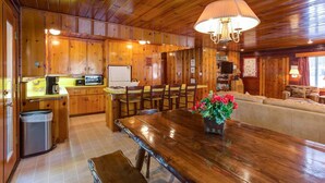 Interno di una baita in legno con tavolo da pranzo, sedie, angolo cottura e soggiorno con divano.