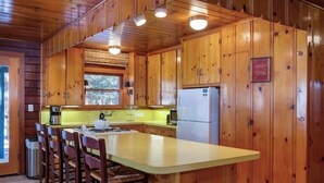 Cucina in stile baita con pareti in legno, isola centrale con sgabelli da bar, frigorifero e finestra sopra il lavello.