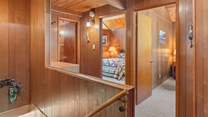 Un interior de madera con una escalera, un espejo y una habitación visible a través de una puerta abierta.