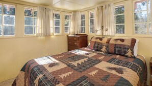 A bedroom with a large bed, multiple windows, and a dresser. - Chatterton's Cottage (Yosemite National Park)