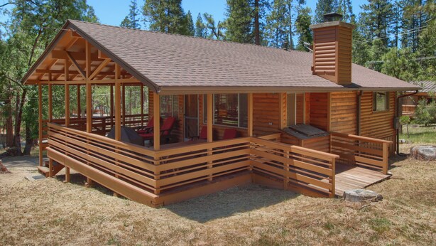 Une cabane en bois dotée d’un porche, d’une cheminée et d’une terrasse couverte.