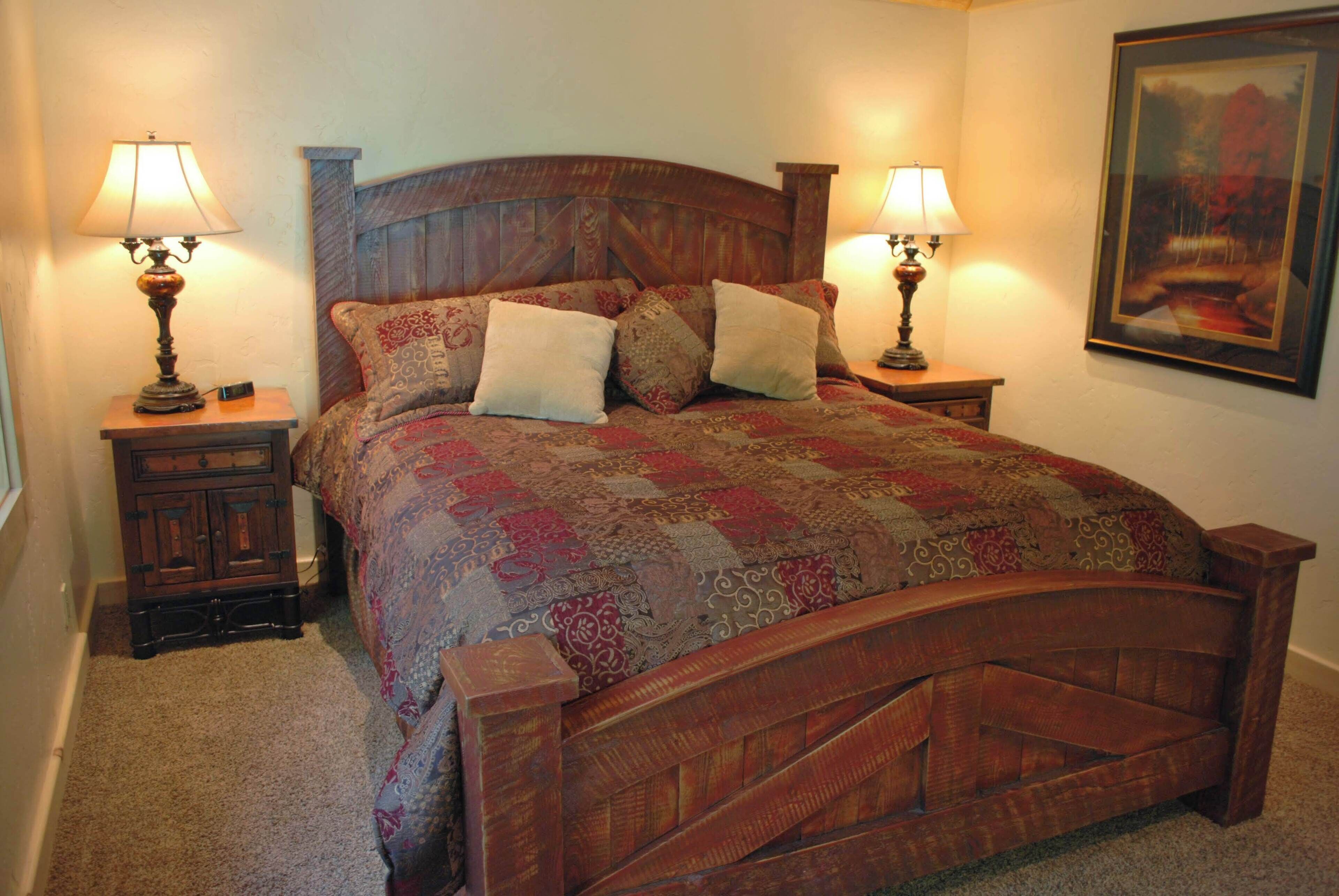 A wooden bed with a quilt, two bedside tables with lamps, and a framed picture on the wall.