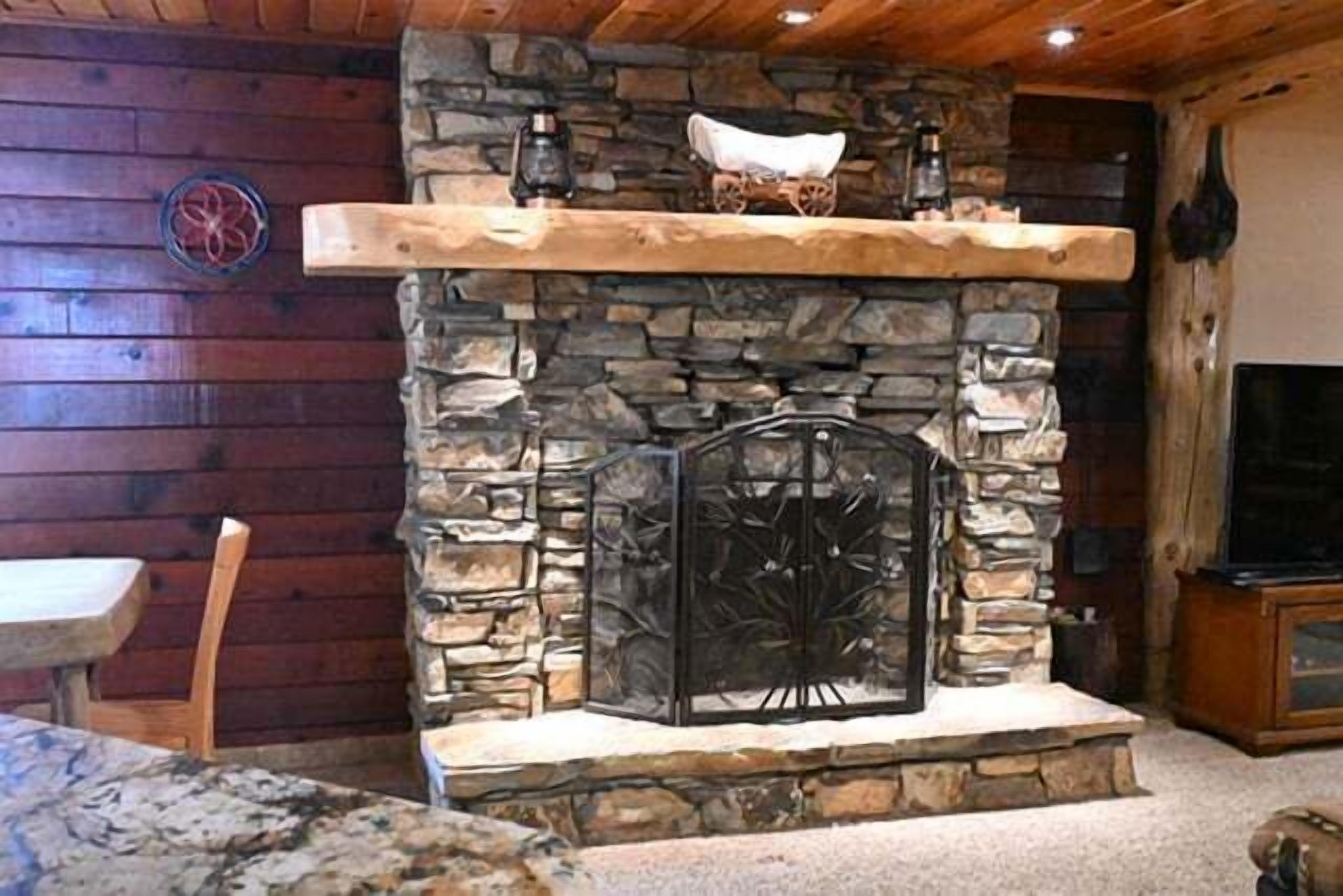 A stone fireplace with a wooden mantel, a stone wall, and a television on a wooden stand.