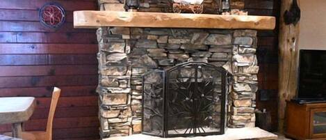 A stone fireplace with a wooden mantel, a stone wall, and a television on a wooden stand.