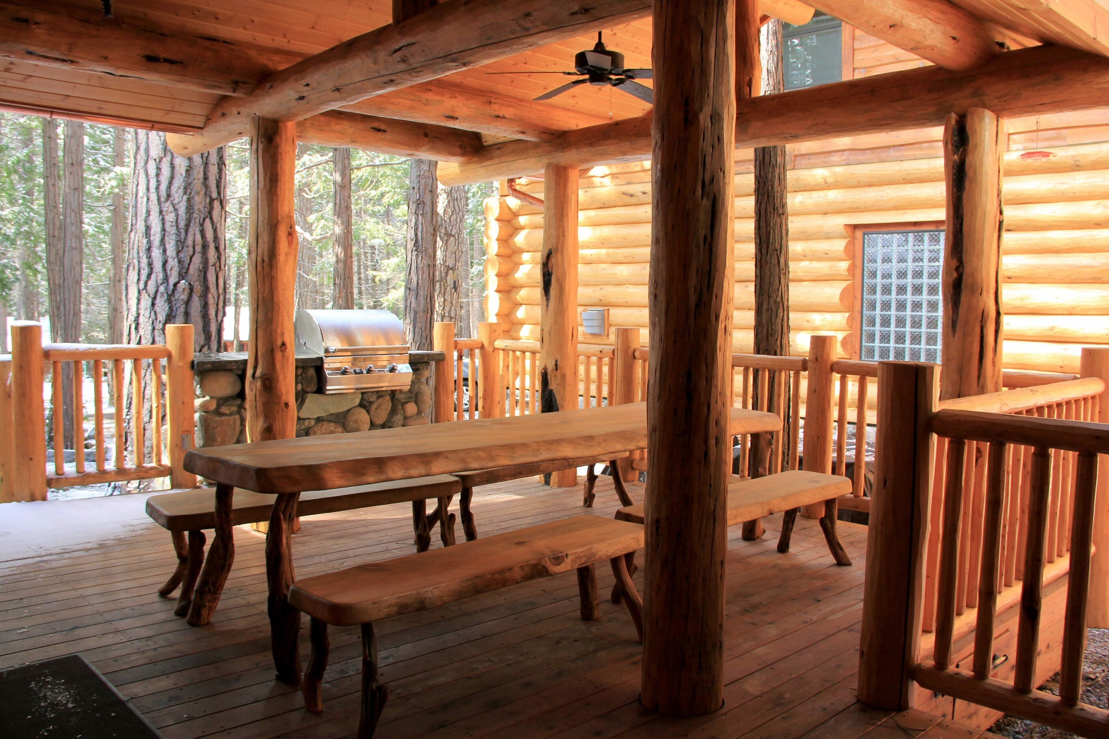 Une cabane en bois dotée d’une terrasse couverte, de tables de pique-nique et d’un barbecue.