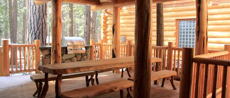 Une cabane en bois dotée d’une terrasse couverte, de tables de pique-nique et d’un barbecue.