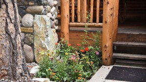 A wooden cabin entrance with a stone wall, a gravel path, and a variety of colorful flowers. - Grizzly Giant (Yosemite National Park)