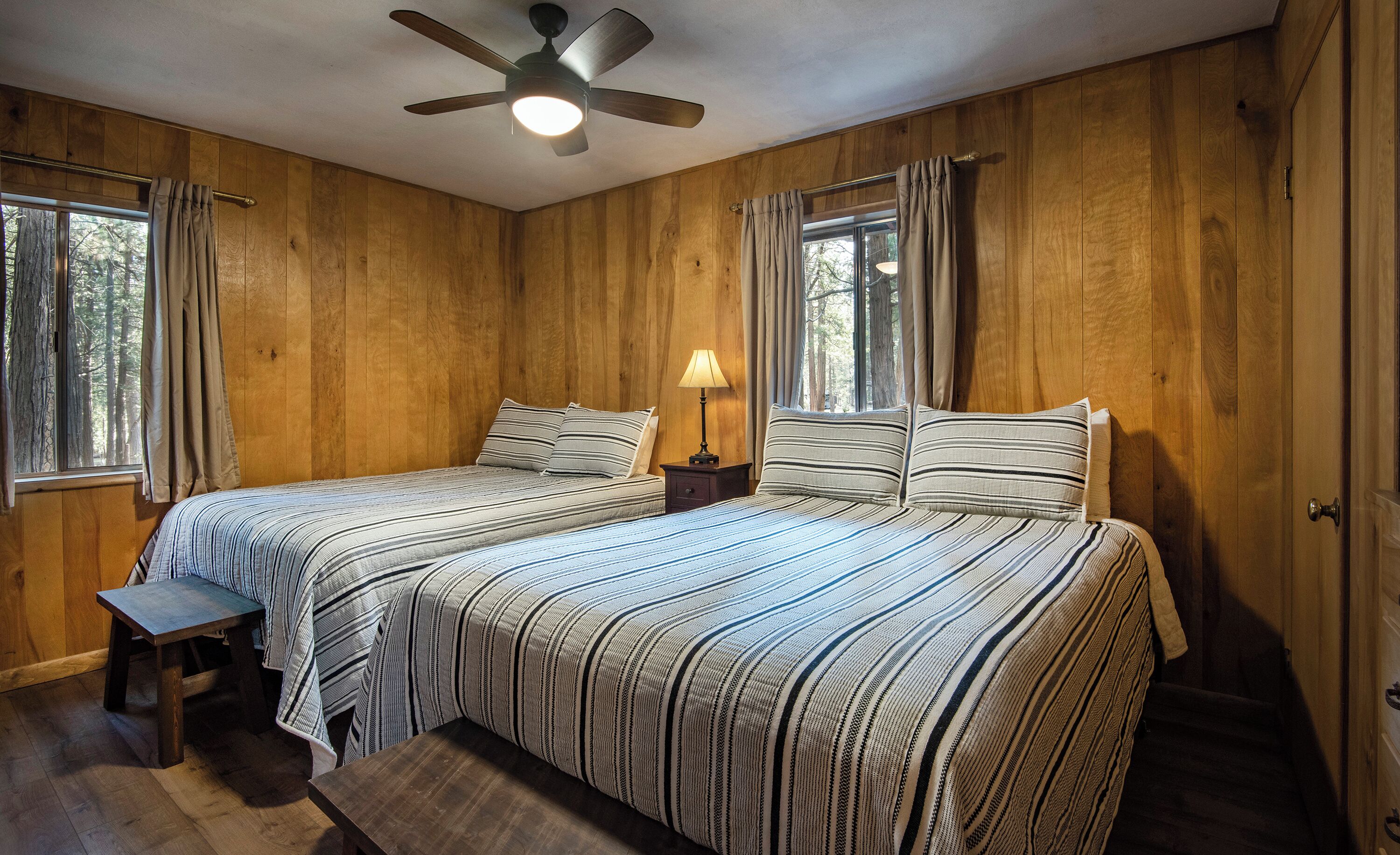 Une chambre avec deux lits, des murs en bois, un ventilateur de plafond et une fenêtre avec des rideaux.