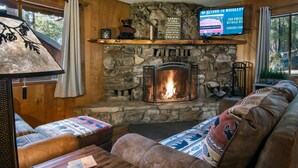 A cozy cabin interior with a stone fireplace, a television mounted above it, and a comfortable seating area with patterned cushions. - Pine Creek Cabin (Yosemite National Park)