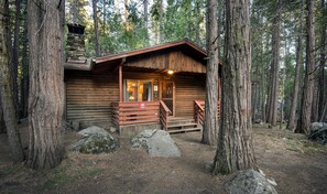 A rustic cabin with a wooden exterior, a porch with wooden railings, and a stone chimney. - Pine Creek Cabin (Yosemite National Park)
