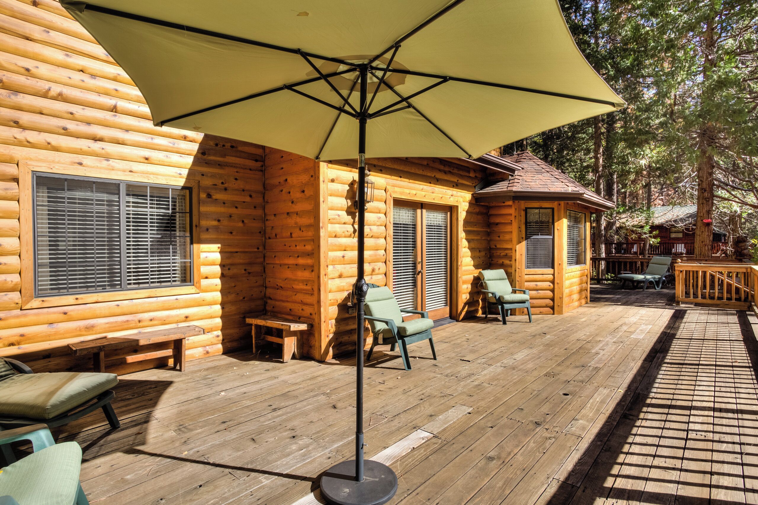 A log cabin with a wooden deck, outdoor seating, and a large umbrella providing shade.
