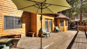 A log cabin with a wooden deck, outdoor seating, and a large umbrella providing shade.