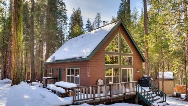 A cabin with a wooden exterior, large windows, a deck, and a snow-covered roof. - Wawona Chalet (Yosemite National Park)