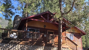Une cabane en rondins avec des fondations en pierre, une terrasse en bois et une cheminée en pierre.
