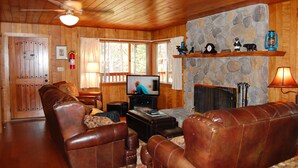 A cozy living room with wooden walls, a stone fireplace, leather sofas, a television, and a ceiling fan. - Harmony Villa (Yosemite National Park)