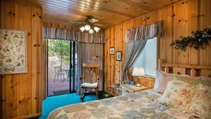 Un dormitorio de cabaña acogedor con techo de madera, una cama con ropa de cama floral, un sillón mecededor y una ventana con cortinas.