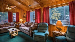 Interior acogedor de una cabaña con paredes de madera, un ventilador de techo, un sofá, una silla y una mesa.