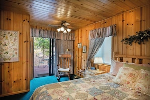 Un dormitorio de cabaña de madera acogedor con una cama, un sillón mecedor, una mesita de noche y un ventilador de techo.
