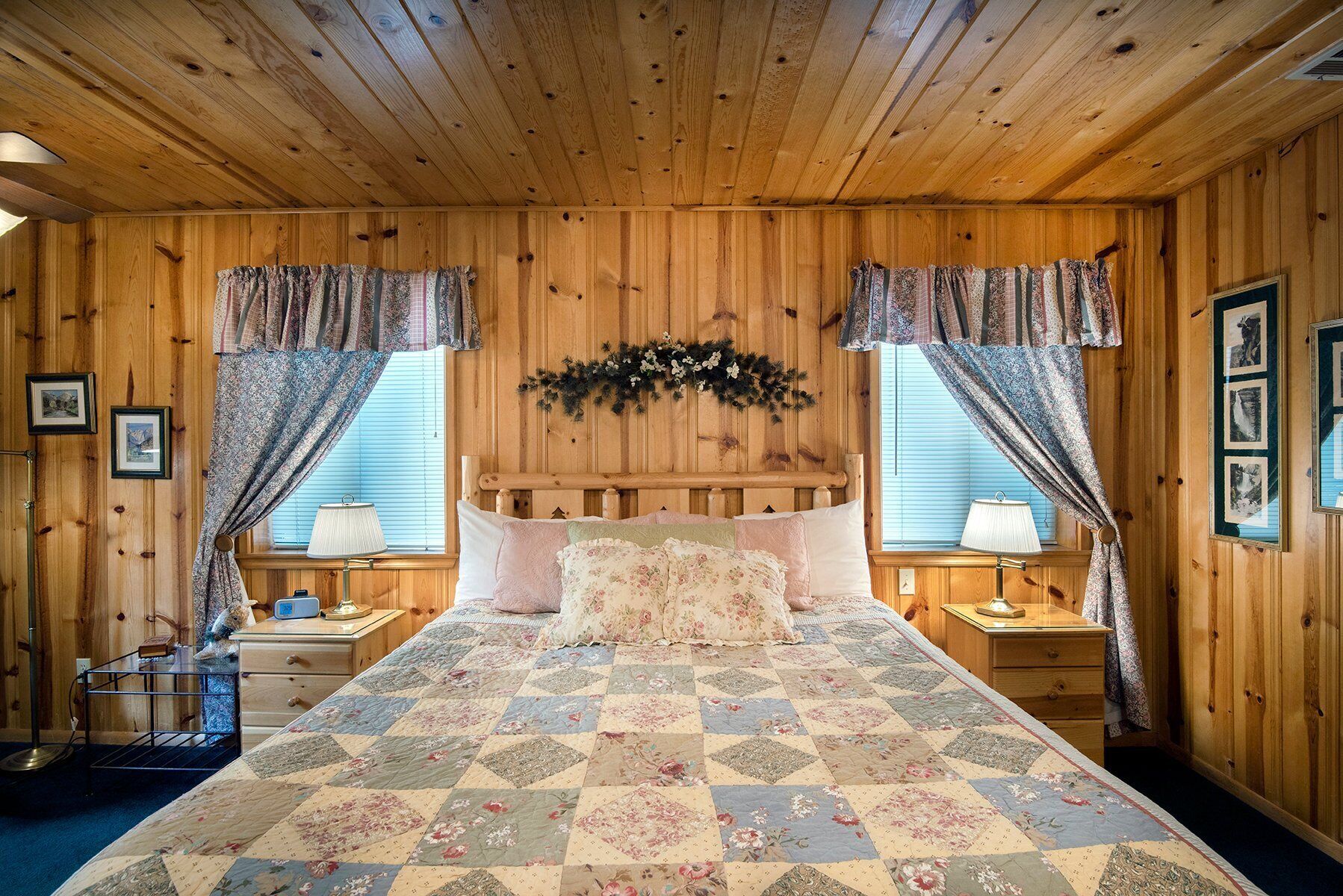 A cozy wooden cabin bedroom with a large bed, two bedside tables, and a headboard with a garland.
