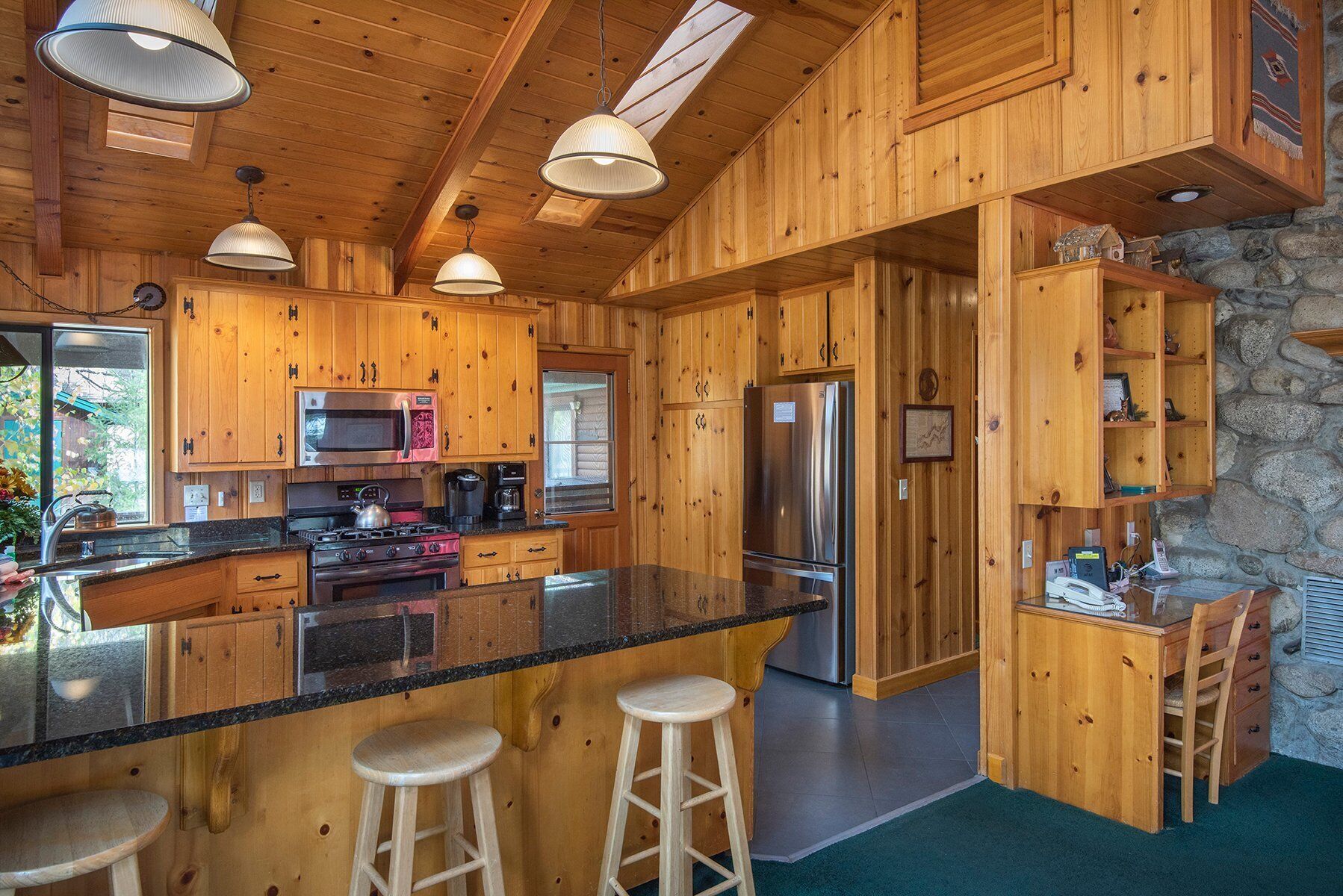 Une cuisine rustique, située dans une cabane en bois, avec un grand îlot central, des tabourets de bar, un réfrigérateur et un mur en pierre.